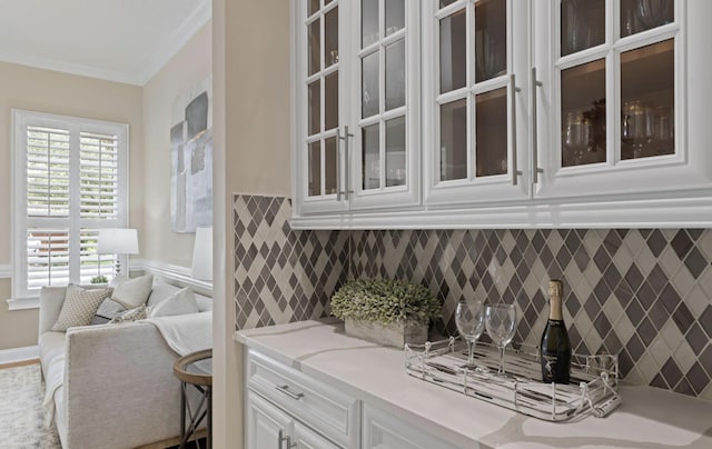 bar with tasteful backsplash, white cabinetry, light stone counters, and ornamental molding