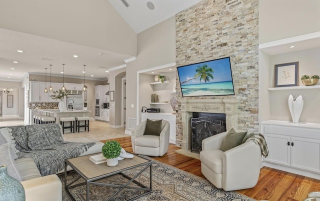 living room featuring high vaulted ceiling, sink, light hardwood / wood-style flooring, built in features, and a fireplace