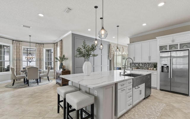 kitchen with appliances with stainless steel finishes, white cabinetry, hanging light fixtures, and an island with sink