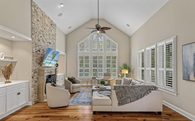 living room featuring high vaulted ceiling, light hardwood / wood-style floors, a stone fireplace, and ceiling fan