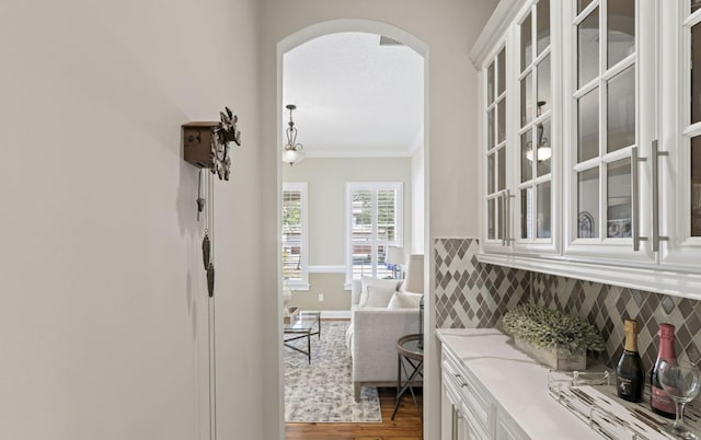 bar with decorative backsplash, ornamental molding, white cabinetry, light stone counters, and wood-type flooring