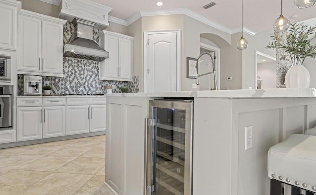 kitchen with wine cooler, stainless steel appliances, wall chimney range hood, white cabinetry, and an island with sink