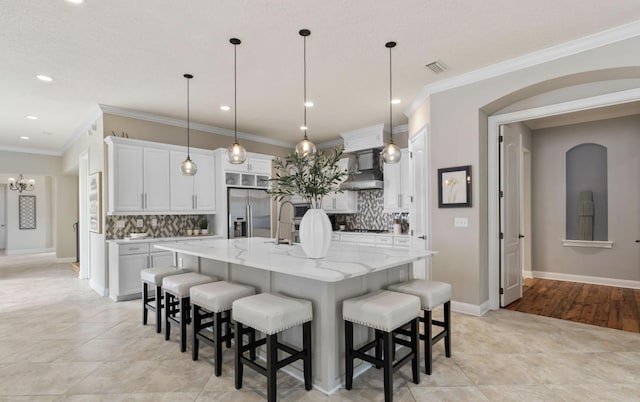 kitchen featuring pendant lighting, a large island with sink, white cabinets, stainless steel fridge, and ornamental molding