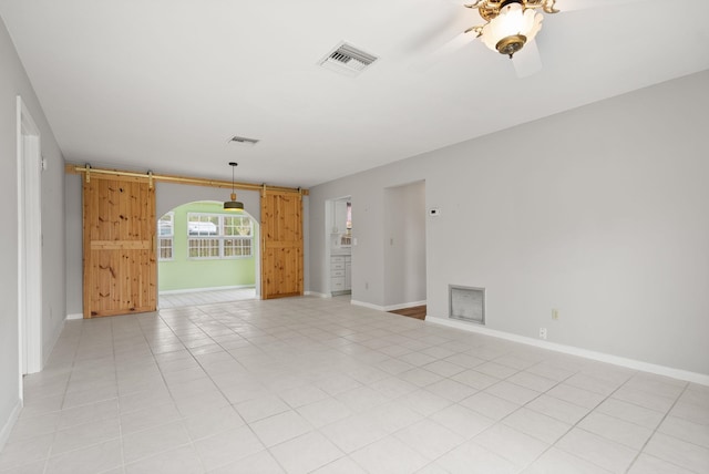 empty room with light tile patterned floors, visible vents, baseboards, and a barn door