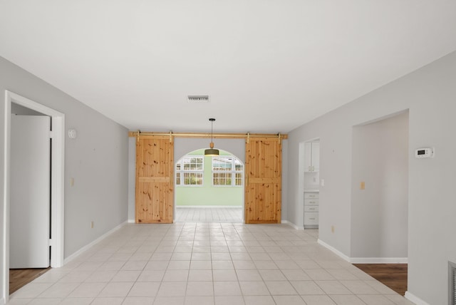 empty room featuring a barn door, visible vents, baseboards, and light tile patterned flooring