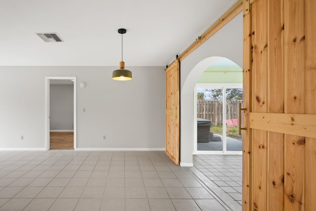 spare room featuring light tile patterned floors, arched walkways, a barn door, visible vents, and baseboards