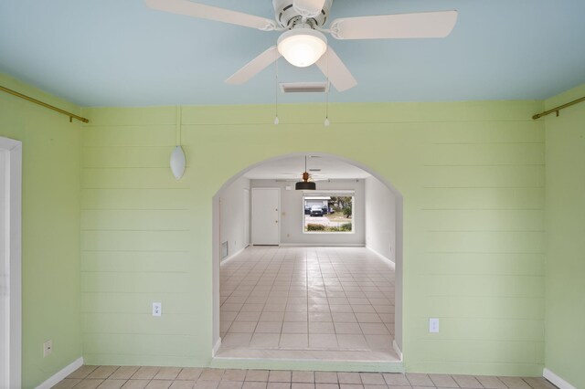 empty room featuring ceiling fan, wooden walls, and arched walkways