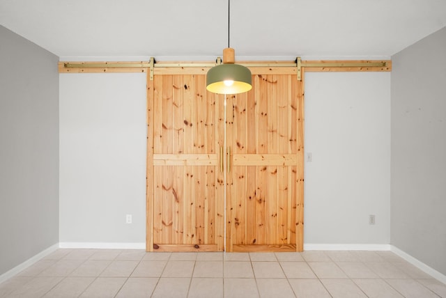 tiled empty room featuring a barn door and baseboards