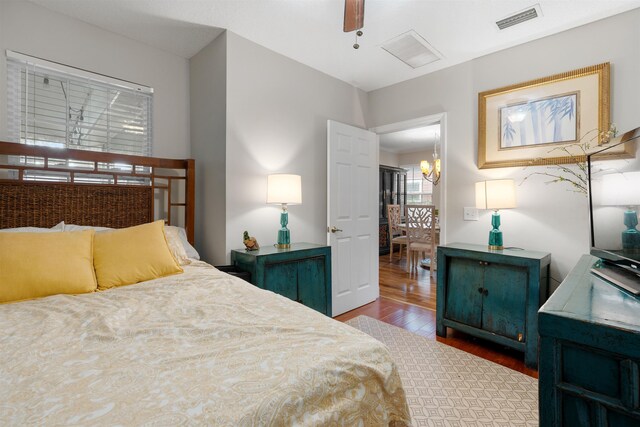 bedroom with ceiling fan with notable chandelier and hardwood / wood-style flooring