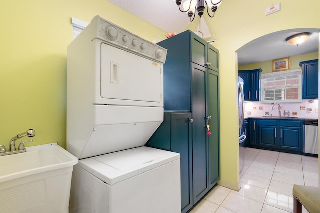 laundry room featuring light tile patterned floors, a textured ceiling, stacked washer and clothes dryer, and sink