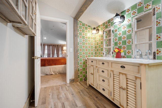 bathroom with a textured ceiling, hardwood / wood-style floors, vanity, and lofted ceiling