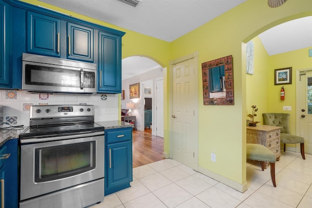 kitchen with light tile patterned floors, stainless steel appliances, blue cabinets, and dark stone counters