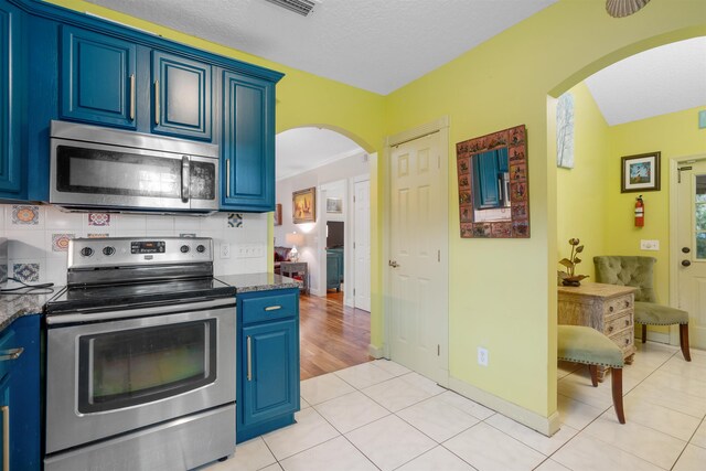 162 Martin Luther King Ave, Saint Augustine, FL 32084 - kitchen featuring appliances with stainless steel finishes, blue cabinetry, arched walkways, tasteful backsplash, and light tile patterned floors