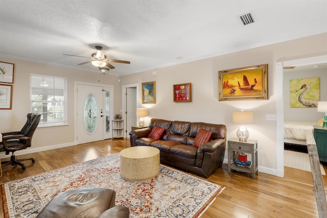 living room with ceiling fan, light hardwood / wood-style floors, a textured ceiling, and ornamental molding