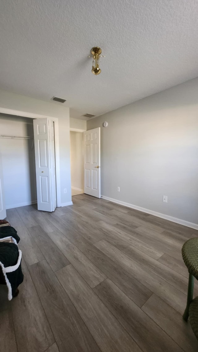 unfurnished bedroom featuring wood finished floors, baseboards, a closet, and a textured ceiling
