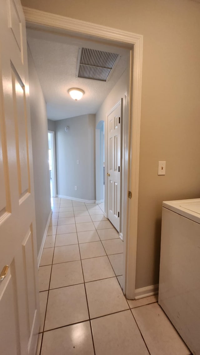 hall with washer / clothes dryer, light tile patterned flooring, and baseboards