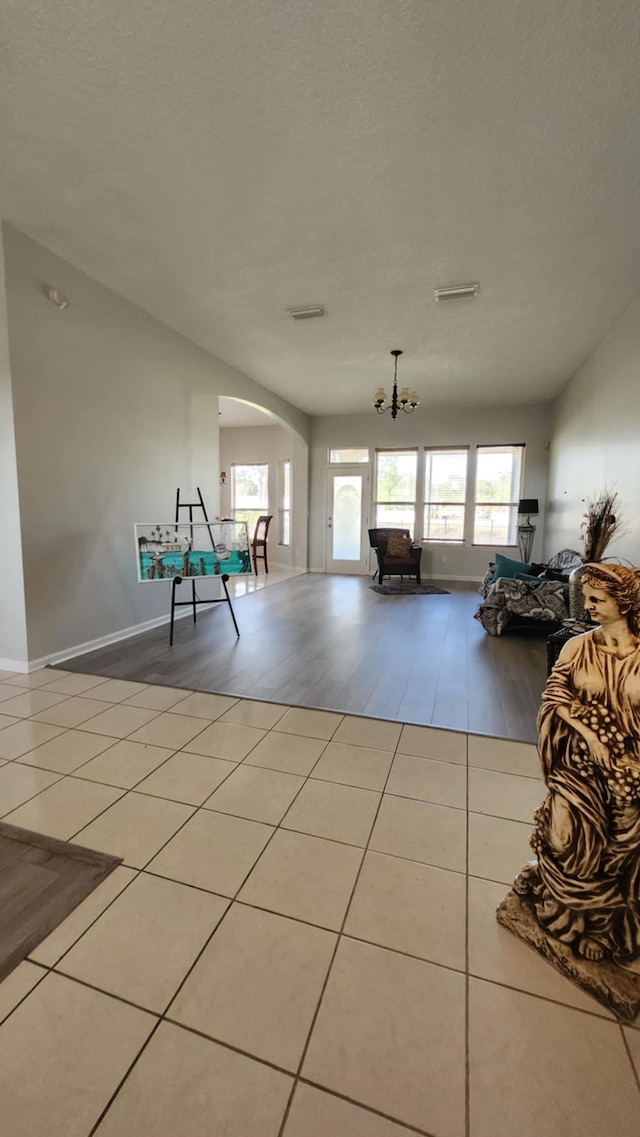 recreation room with arched walkways, healthy amount of natural light, tile patterned flooring, and a chandelier