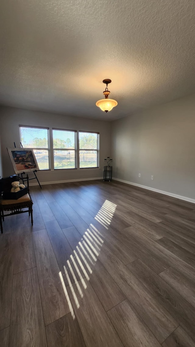 living area featuring dark wood-type flooring, healthy amount of natural light, a textured ceiling, and baseboards
