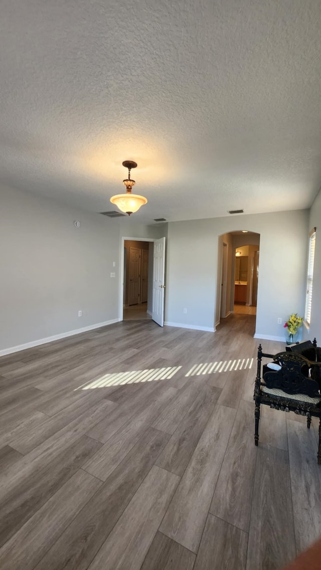 living area with arched walkways, wood finished floors, baseboards, and a textured ceiling