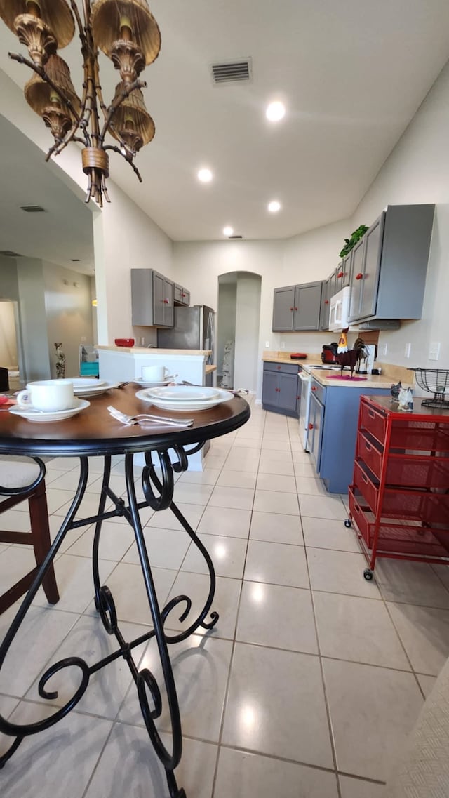 kitchen with gray cabinets, white appliances, arched walkways, light tile patterned floors, and recessed lighting