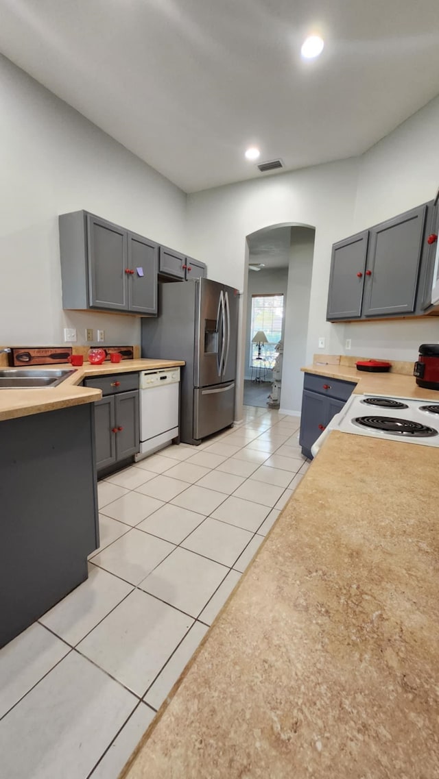 kitchen with arched walkways, a sink, white dishwasher, light tile patterned floors, and stainless steel fridge with ice dispenser