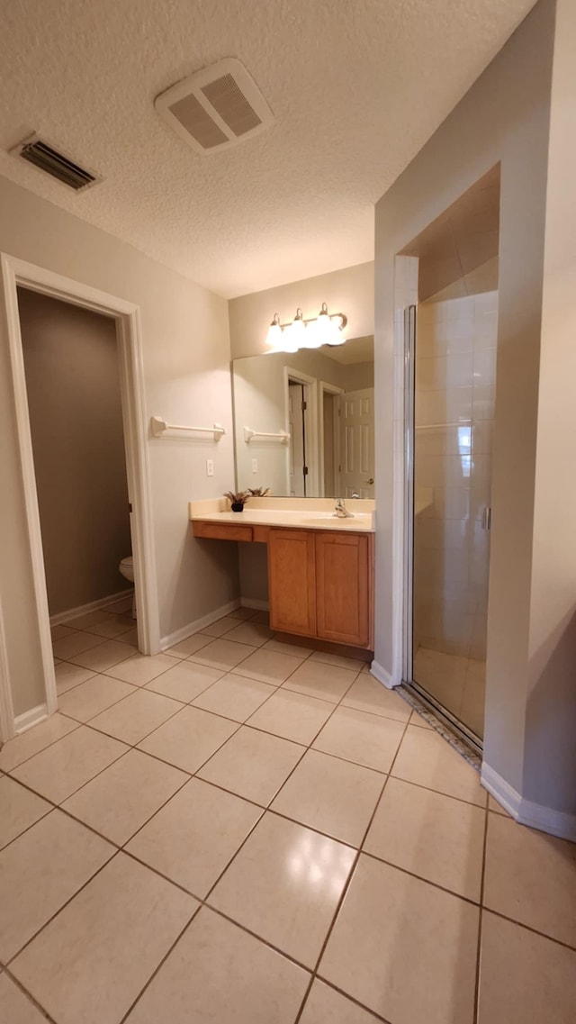 bathroom featuring a stall shower, tile patterned flooring, a textured ceiling, double vanity, and toilet