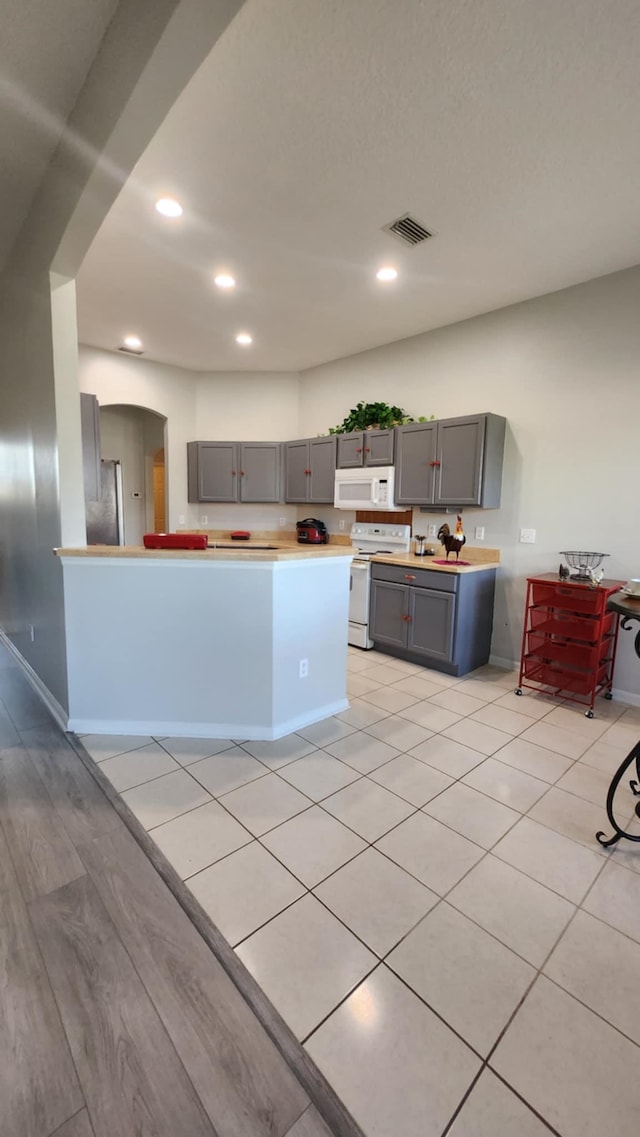 kitchen featuring gray cabinetry, white appliances, recessed lighting, light countertops, and arched walkways