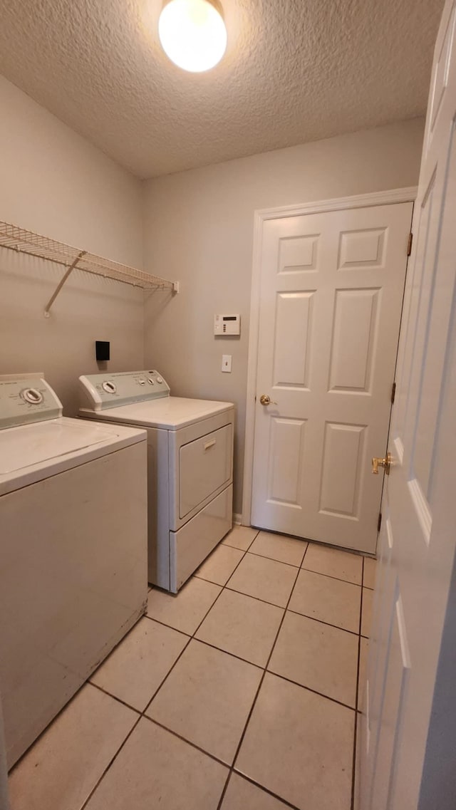 laundry area with washer and dryer, a textured ceiling, and light tile patterned floors