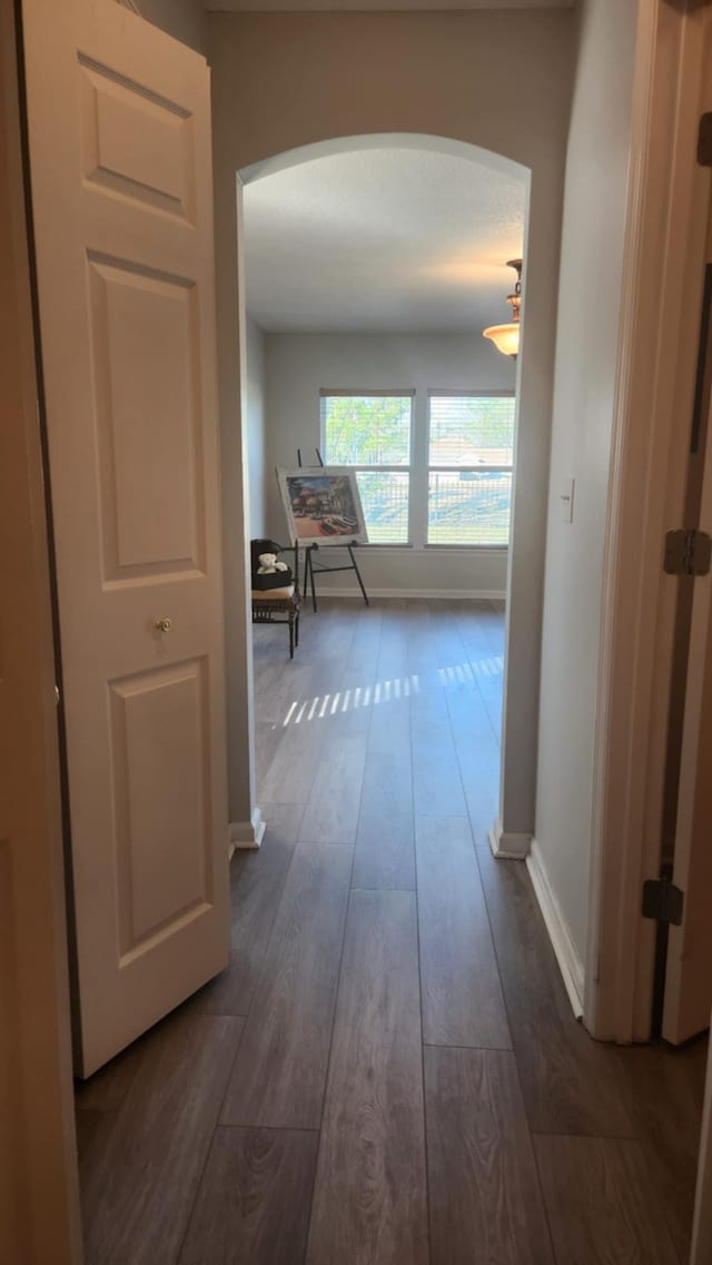 hall featuring arched walkways, dark wood-style floors, and baseboards