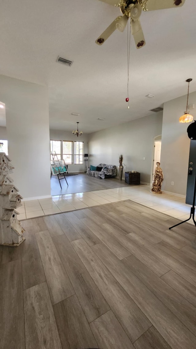 unfurnished living room with wood finished floors, ceiling fan, baseboards, and a chandelier