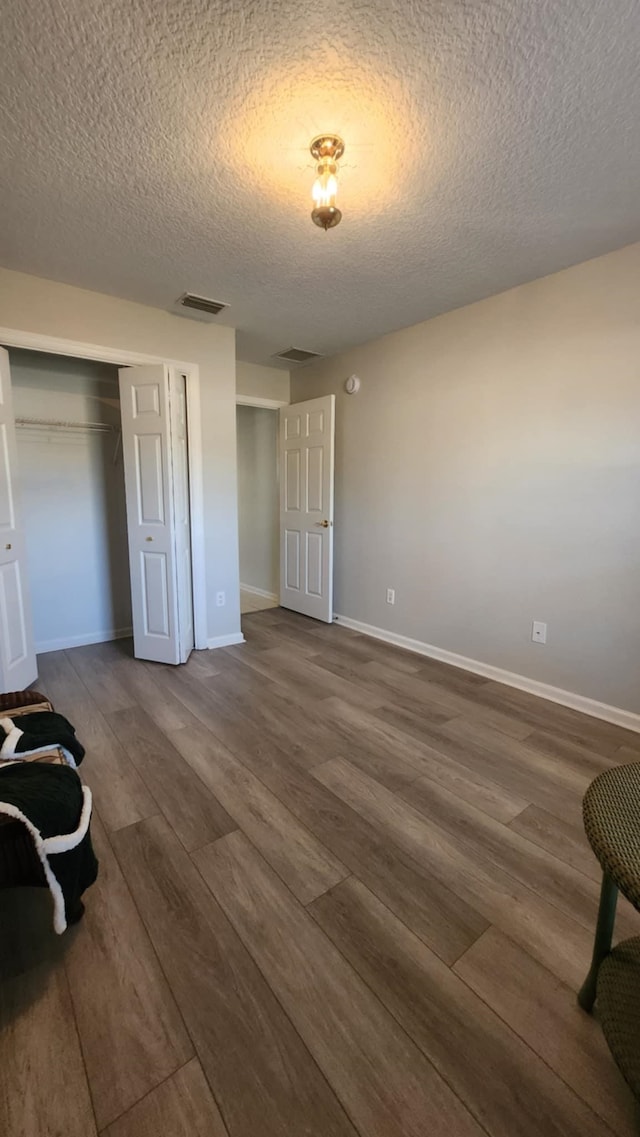unfurnished bedroom with dark wood-style flooring, a closet, a textured ceiling, and baseboards