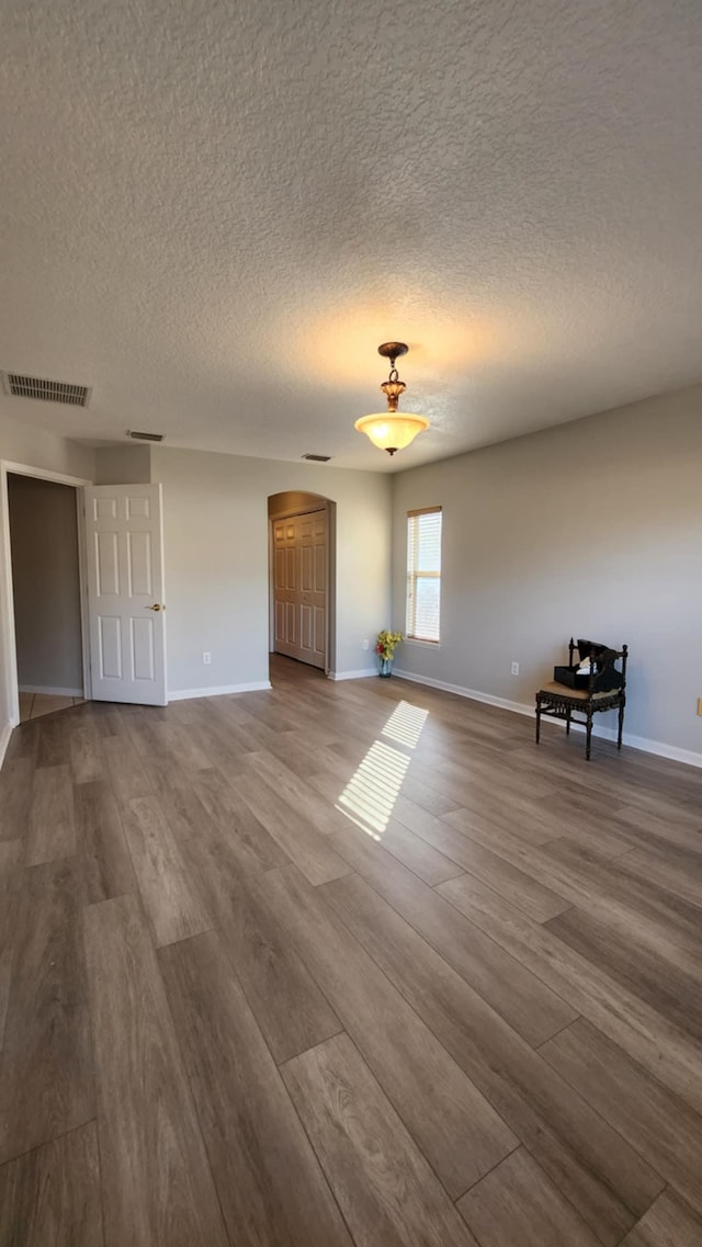 empty room with dark wood-style floors, baseboards, arched walkways, and a textured ceiling
