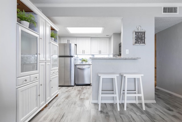 kitchen with white cabinetry, light stone counters, light hardwood / wood-style floors, a textured ceiling, and appliances with stainless steel finishes