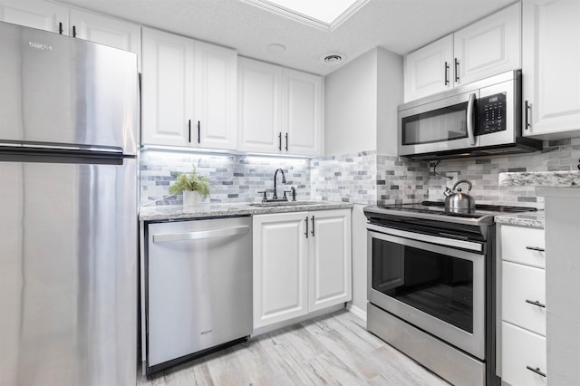 kitchen with light wood-type flooring, backsplash, stainless steel appliances, sink, and white cabinets