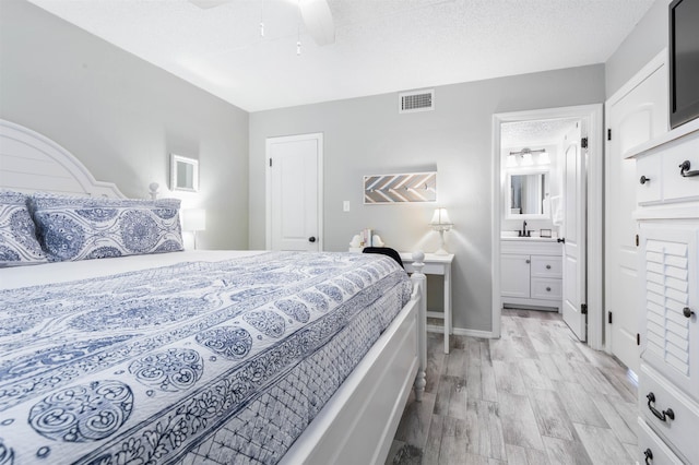 bedroom featuring sink, ensuite bath, ceiling fan, light wood-type flooring, and a textured ceiling