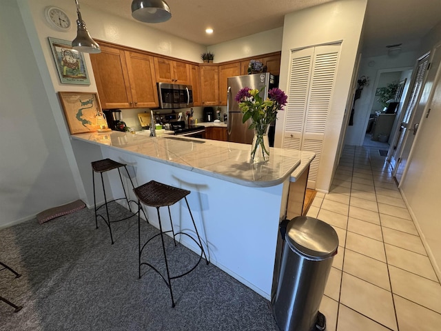 66 Village Del Lago Cir, Saint Augustine, FL 32080 - kitchen with light tile patterned flooring, a breakfast bar area, appliances with stainless steel finishes, a peninsula, and brown cabinets
