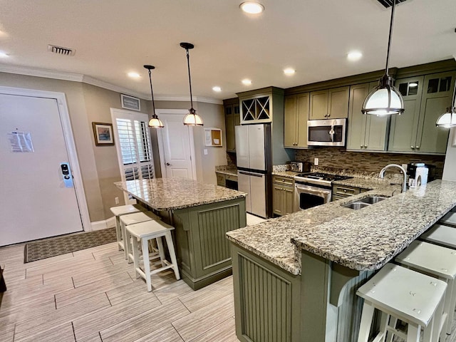 kitchen with a sink, hanging light fixtures, appliances with stainless steel finishes, a center island, and green cabinetry