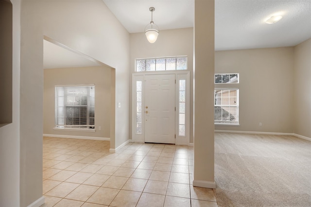 foyer featuring a textured ceiling, light colored carpet, and a high ceiling