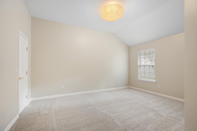 spare room with a textured ceiling, light colored carpet, and lofted ceiling