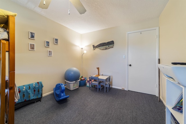 recreation room with ceiling fan, dark carpet, and a textured ceiling