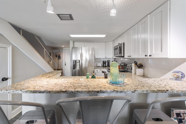 kitchen with backsplash, white cabinets, a kitchen bar, and appliances with stainless steel finishes