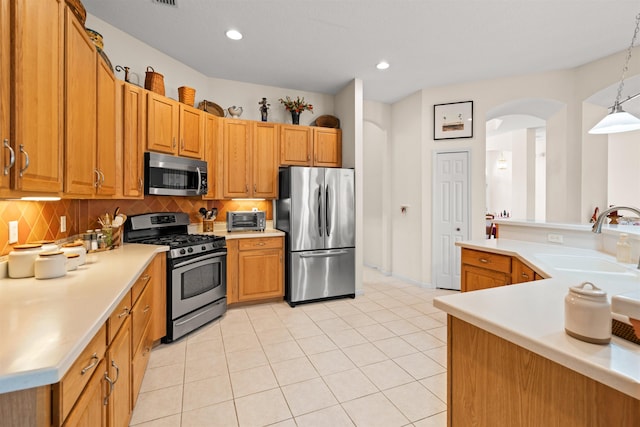 kitchen with appliances with stainless steel finishes, sink, light tile patterned floors, and decorative light fixtures