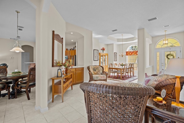 living room featuring a tray ceiling, a textured ceiling, a chandelier, and light tile patterned flooring