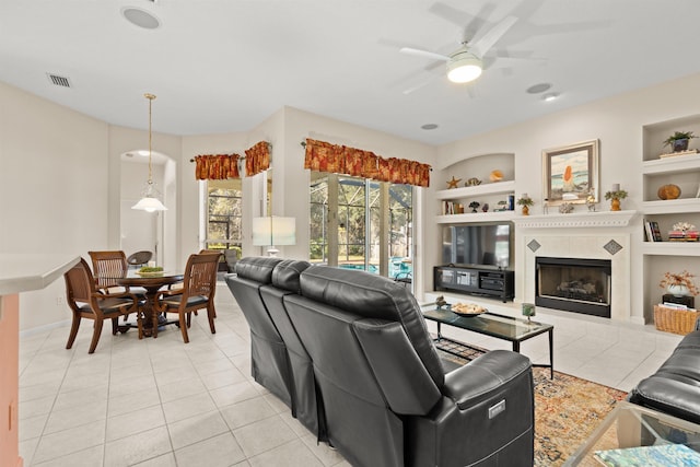 tiled living room with built in features, a tile fireplace, and ceiling fan