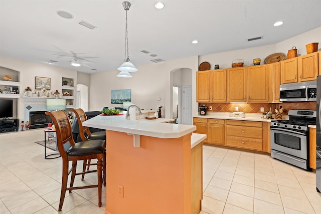 kitchen with a kitchen bar, decorative light fixtures, light tile patterned floors, appliances with stainless steel finishes, and a kitchen island with sink