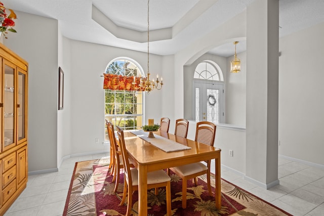 dining area featuring a raised ceiling, a wealth of natural light, light tile patterned floors, and a chandelier