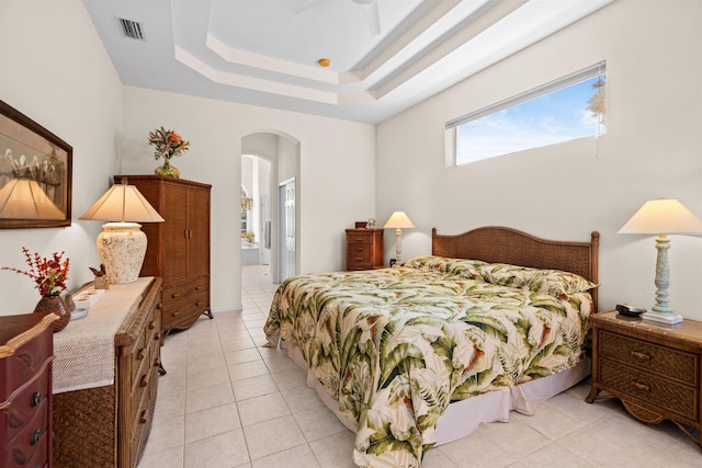 tiled bedroom featuring a tray ceiling, ensuite bath, and ceiling fan