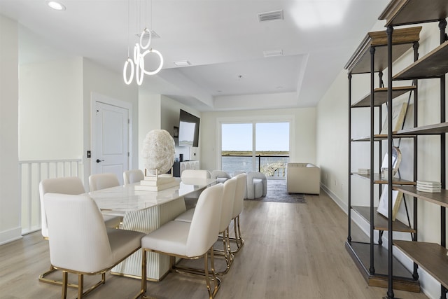 dining area featuring a notable chandelier, light hardwood / wood-style floors, and a raised ceiling