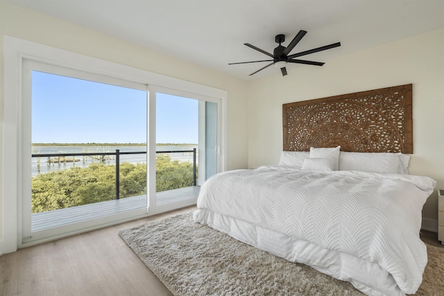 bedroom with access to exterior, hardwood / wood-style floors, a water view, and ceiling fan