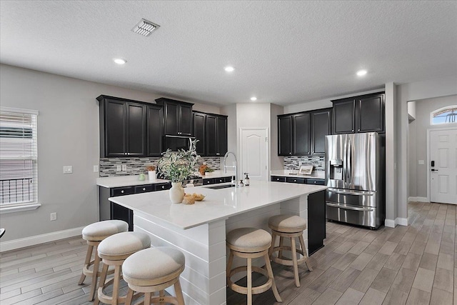 kitchen with visible vents, a sink, dark cabinetry, stainless steel fridge, and light countertops